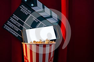 Mobile phone with empty white bright screen with popcorn bucket and movie clapper board. Concept of streaming TV on internet phone