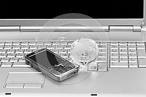 Mobile phone and glass globe on laptop keyboard