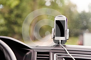 Mobile phone with GPS card in the car. A white smartphone on a stand in the car is used for navigation.