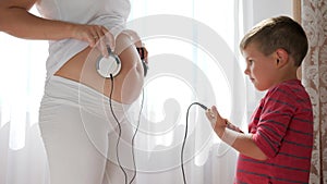 Mobile phone in hands of little boy standing with pregnant female which holds headphones on stomach