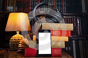 Mobile phone, headphones and a stack of books near the lamp. Concept of training and audiobooks. Library bookcase in the