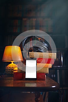 Mobile phone, headphones and a stack of books near the lamp. Concept of training and audiobooks. Library bookcase in the