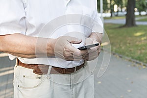 A mobile phone in the large hands of an elderly man in a white shirt on a walk in the park