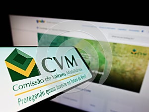 Mobile phone with logo of Brazilian Comissao de Valores Mobiliarios (CVM) on screen in front of website.