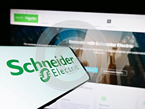 Mobile phone with logo of French company Schneider Electric SE on screen in front of business website.