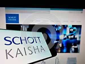 Mobile phone with logo of Indian packaging company Schott Kaisha Pvt. Ltd. on screen in front of website.