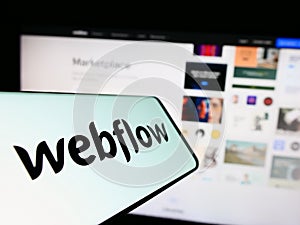 Mobile phone with logo of US web development software company Webflow Inc. on screen in front of website.