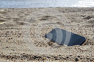 Mobile phone lying on the beach in the sand. weatherproof phones, lost phone concept