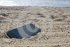 Mobile phone lying on the beach in the sand. weatherproof phones, lost phone concept, data loss a photo