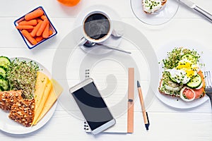 Mobile phone, planning notebook and healthy breakfast. Day diet planning and healthy eating concept. Sandwich with egg benedict, o