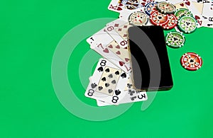 Mobile phone and poker chips with playing cards on a green table. online casino concept.