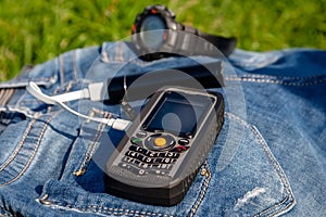 A mobile phone and a power bank on a jeans on background clock.