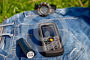 A mobile phone and a power bank on a jeans on background clock.