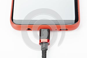 Mobile phone in a red case with a connected cable for charging power on a white background