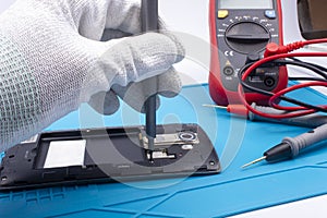 Mobile phone repair. The service technician disassembles the phone on the esd mat with a screwdriver photo