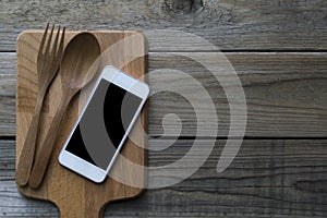 Mobile phone served wiht fork and spoon on wood plate