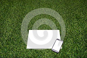 Mobile phone and sheet of paper lying on the grass