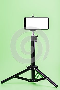Mobile phone on a tripod with a clear white display for images and text, green isolated background