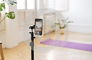 Mobile phone on tripod in empty living room with fitness mat on the floor