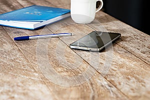 Mobile phone on vintage wooden table with blurred coffee cup and notebook