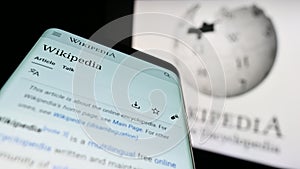 Mobile phone with webpage of online encyclopedia Wikipedia on screen in front of logo.