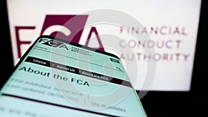 Mobile phone with website of British Financial Conduct Authority (FCA) on screen in front of logo.