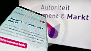 Mobile phone with website of Dutch regulator Autoriteit Consument en Markt (ACM) on screen in front of logo.