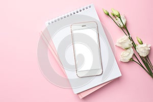 Mobile phone, white eustoma flower and notebook on pink background. Women`s business technology composition
