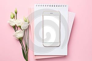 Mobile phone, white flower and notebook on pink background. Women`s business technology composition