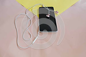 Mobile phone and white headsets on a yellow and pink background