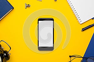 Mobile phone with white notepad , blue notebook and pen on yellow background