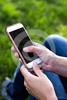 Mobile phone in woman's hand in a deckchair against the background of green grass. Time to rest.