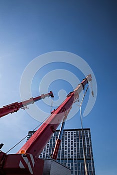 mobile red crane with risen boom. Truck cranes with big telescopic boom and hook suspension above blue sky