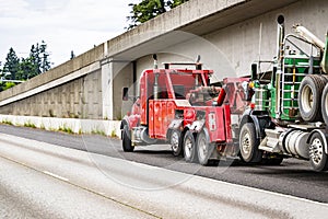 Mobile road assistant red big rig tow semi truck towing broken green semi truck picking up it on the highway road shoulder