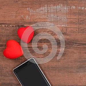 Mobile smart phone with black screen and two red hearts on wooden textured background, empty copy space. Flat lay, top view