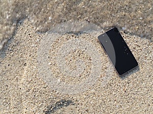 Mobile smart phone falling on the sandy beach with soft waves of sea background.