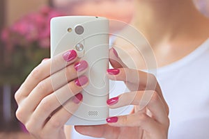 Mobile smart phone in female hands with a pink manicure on the b