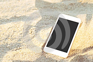 Mobile smart phone put drop on tropical sand beach with sunlight  texture  background. display black copy space of technology.