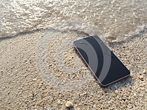 Mobile smart phone on the sandy beach with soft waves of sea background. Summer vacations concept.