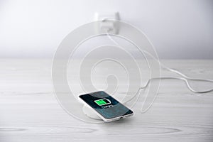 Mobile smart phone on wireless charging device on white background. Icon battery and charging progress lighting on screen.