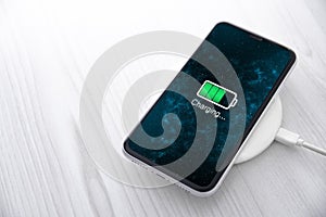 Mobile smart phone on wireless charging device on white background. Icon battery and charging progress lighting on screen.