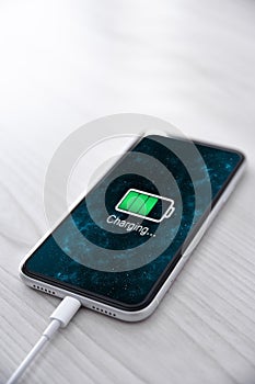 Mobile smart phone on wireless charging device on white background. Icon battery and charging progress lighting on screen.