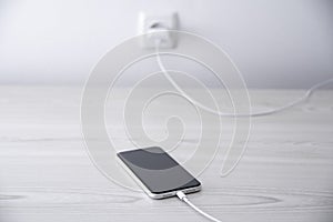 Mobile smart phone on wireless charging device on white background. Icon battery and charging progress lighting on screen.