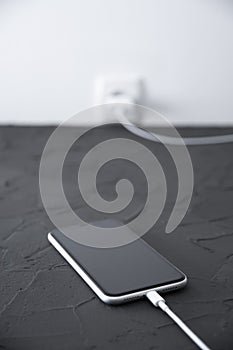 Mobile smart phone on wireless charging device on white background. Icon battery and charging progress lighting on screen.