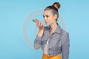 Mobile smart voice technology. Beautiful fashionably dressed woman with hair bun talking to smartphone using virtual assistant
