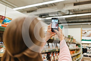 Mobile and social network. lond woman taking a selfie on smartphone in the grocery store. Rear view from the head photo