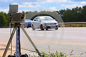 Mobile speed camera device working on summer daytime road with blurry white car in background