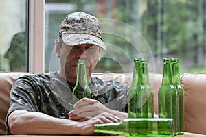 Mobilized soldier in uniform with a bottle of beer in his hand, many empty bottles. Concept: war veteran, family problems, photo