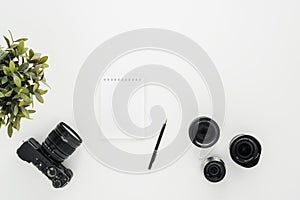 Mocap work photographer on a white table. Flat lay mirrorless camera, a few lenses and a notebook with a pen.