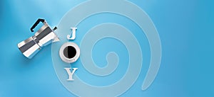 Mocha coffee maker and coffee cup on the inscription JOY made up over blue background.
